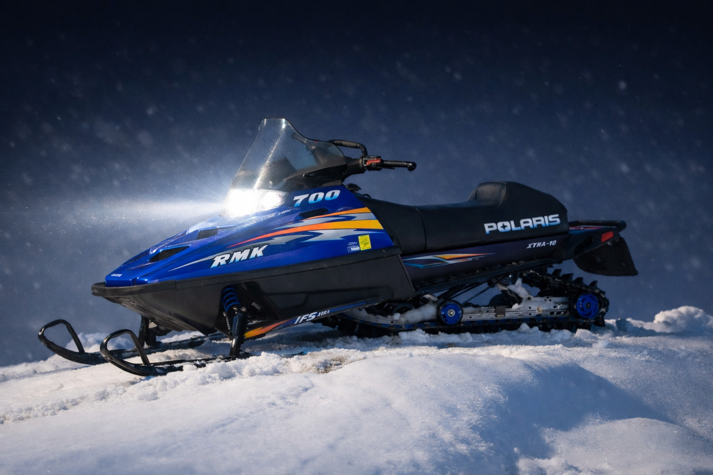 Blue 1999 Polaris Indy RMK 700 snowmobile with bright white LED headlight upgrade at night on snow-covered hill By LEDPowersport