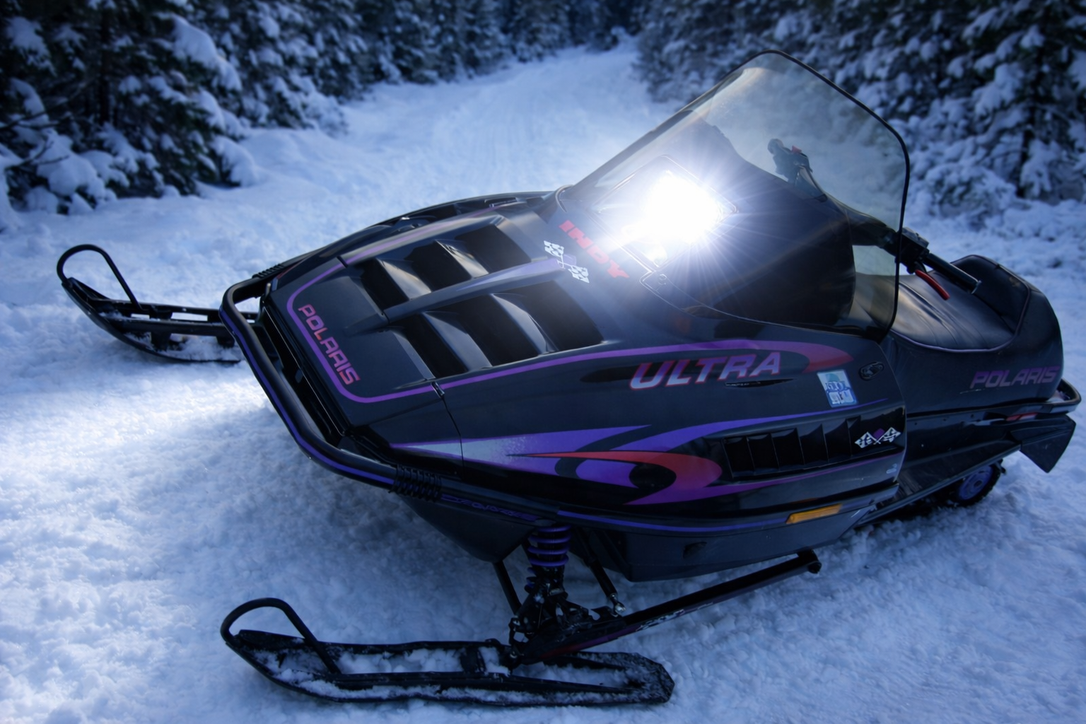 1996 Polaris Ultra SKS snowmobile on wooded trail at dusk with bright white LED headlight upgrade illuminating snowy path By LEDPowersport