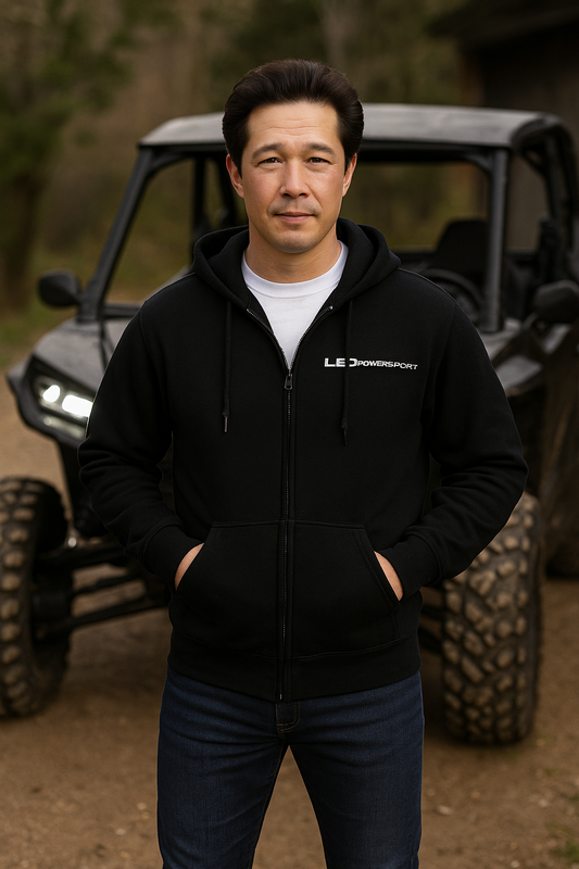 Man wearing black LEDPowersport full-zip hoodie standing in front of a rugged UTV on a dirt trail; logo visible on chest, outdoor riding scene.